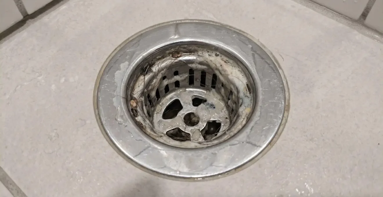 Macro view of a bathroom drain strainer showing accumulated hair and soap residue buildup around the opening